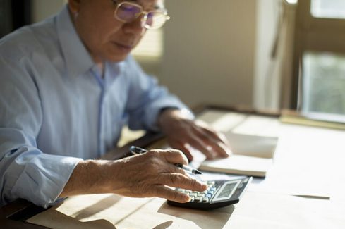 Taiwanese senior man sitting at table and calculating finances